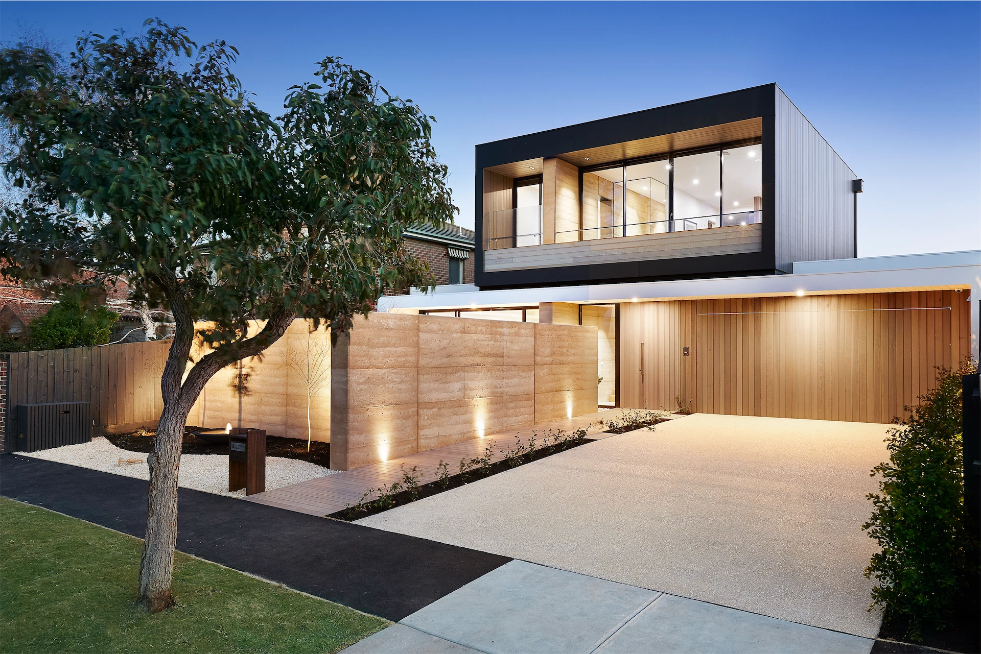 Modern luxury home exterior at dusk with large windows, warm architectural lighting, and natural wood details by a custom home builder